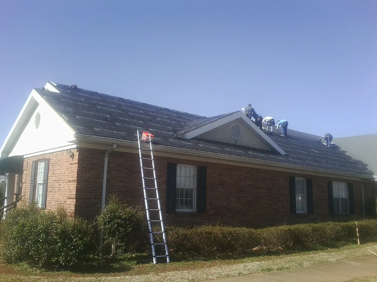 Crew tearing shingles off a brick ranch roof with a ladder set — Metal Roof Repair work by our crew in Cumberland