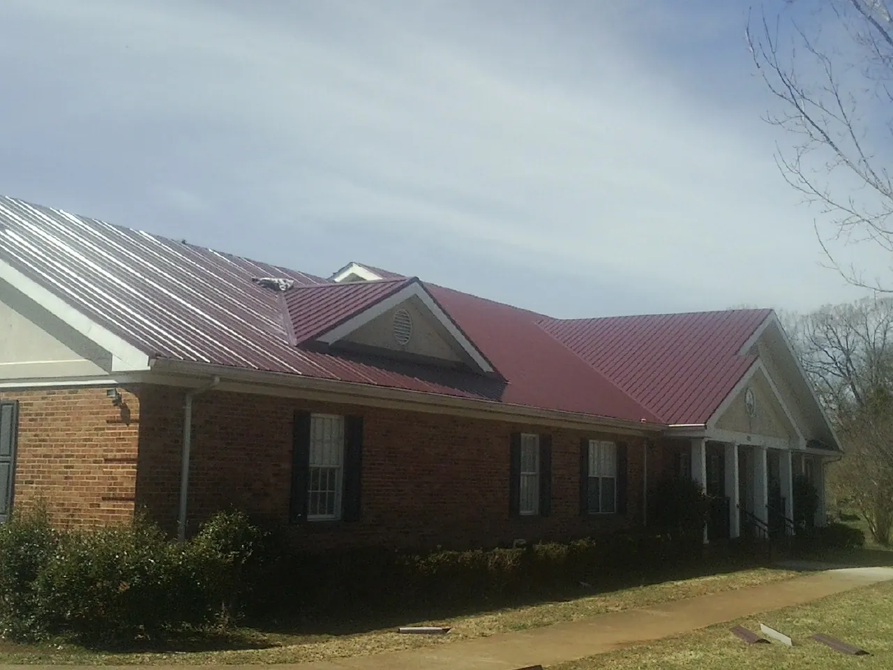 Red metal roof with gabled entries on a long brick building, from a Hail Damage Roof Repair job in Cumberland