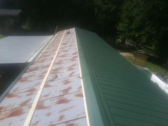 Old rusted panels beside newly installed green metal roofing — Wind Damage Roof Repair by Roofing Brothers in Cumberland